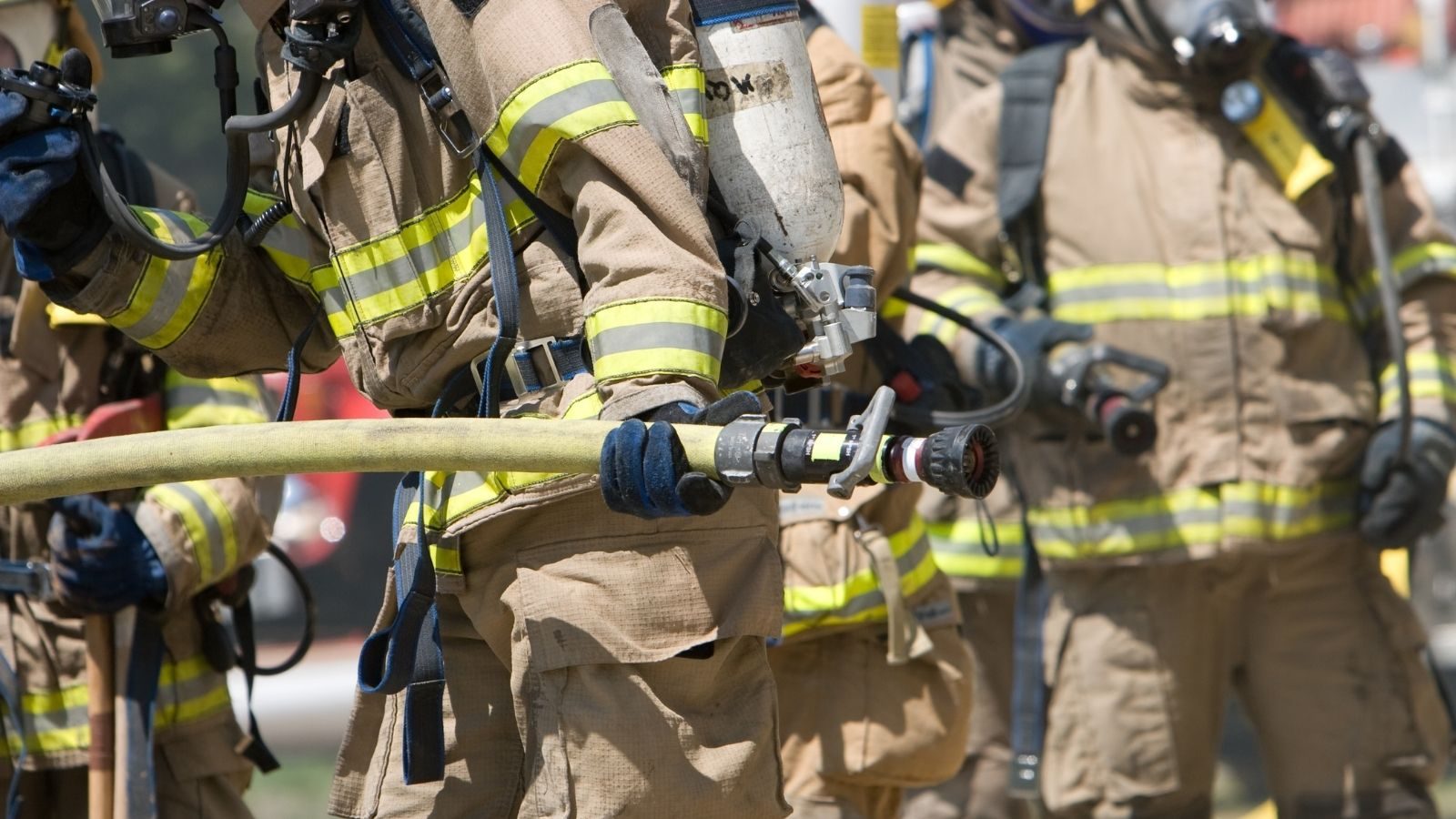 Firefighters in gear holding a hose
